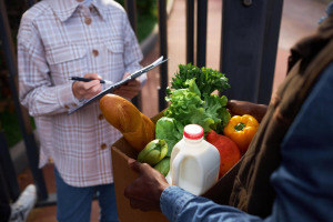 close-up-delivery-man-handing-box-with-fresh-groceries-woman-outdoors_236854-49107